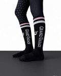 Black knee-high athletic socks with white and pink striped cuffs, featuring the words 'GRAND PARADE' in white, shown on a model's legs against a white and dark gray background.